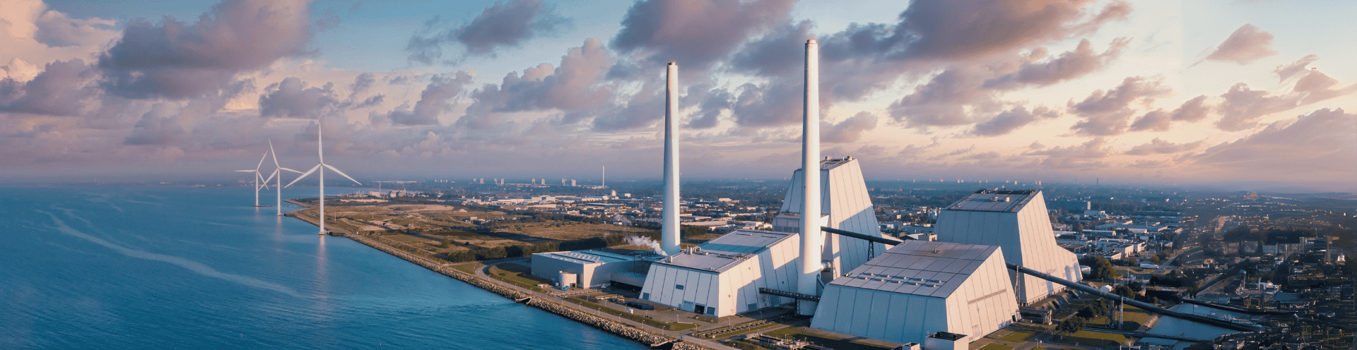 Vista panorâmica de usina de recuperação energética ao lado do mar, com turbinas eólicas
        ao fundo, representando soluções sustentáveis para resíduos sólidos.