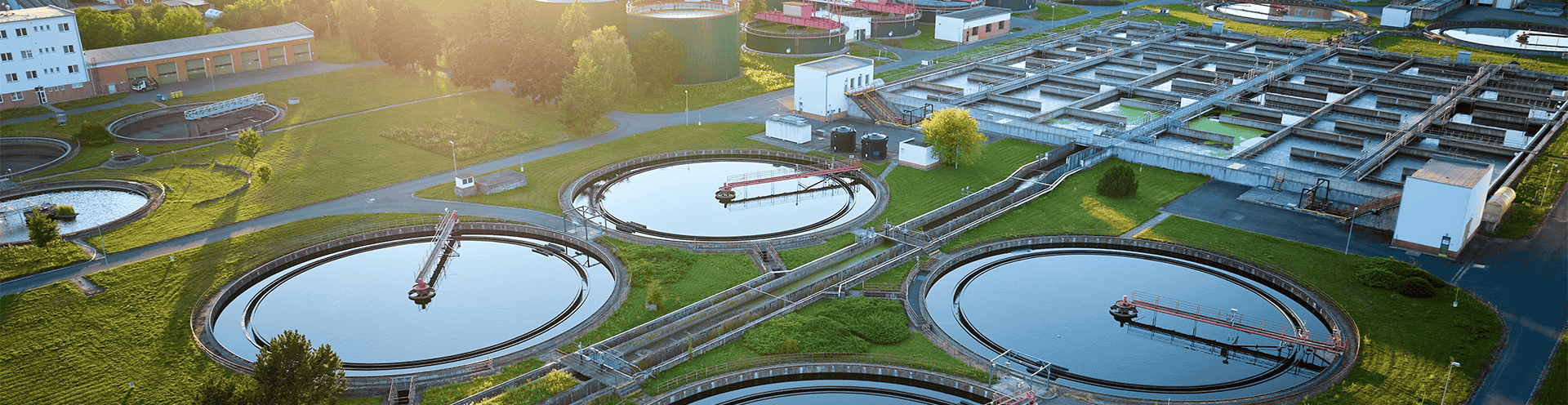 Vista aérea de estação de tratamento de água e esgoto com tanques circulares e estruturas de filtragem, 
        representando a infraestrutura de saneamento básico.