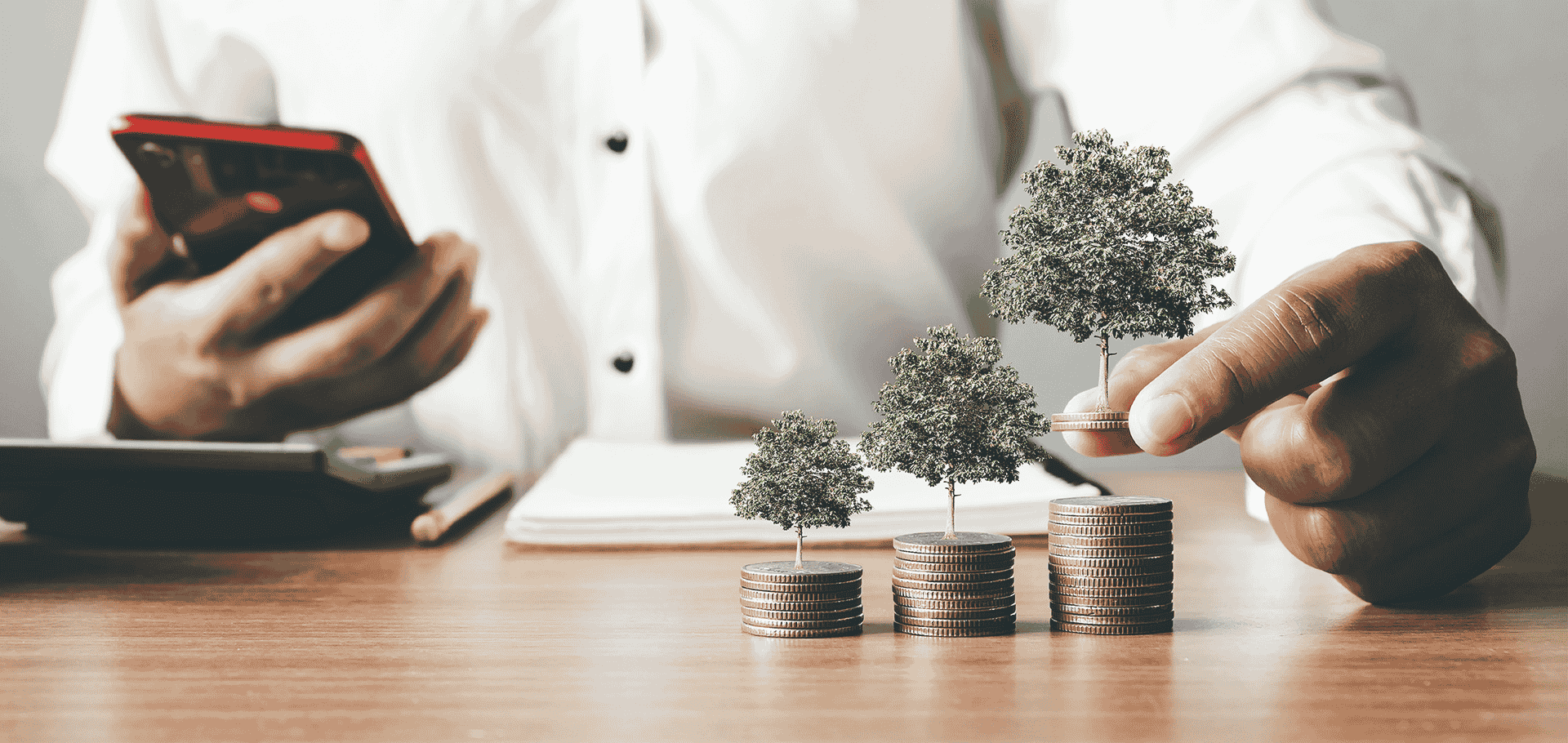Mão de executivo empilha moedas com broto verde nascendo, representando 
         o crescimento de investimentos sustentáveis guiados por critérios ESG.