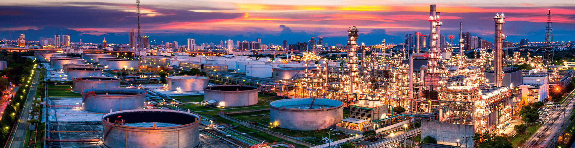 Complexo industrial de refino de petróleo iluminado ao entardecer, com tanques de armazenamento e torres de processamento,
        representando a infraestrutura energética brasileira.
