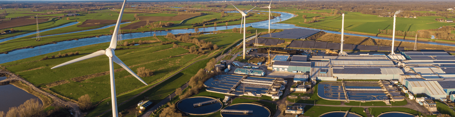 Vista aérea de estação de tratamento de água com turbinas eólicas ao lado de um rio, 
        representando o papel da indústria na gestão integrada e sustentável dos recursos hídricos.